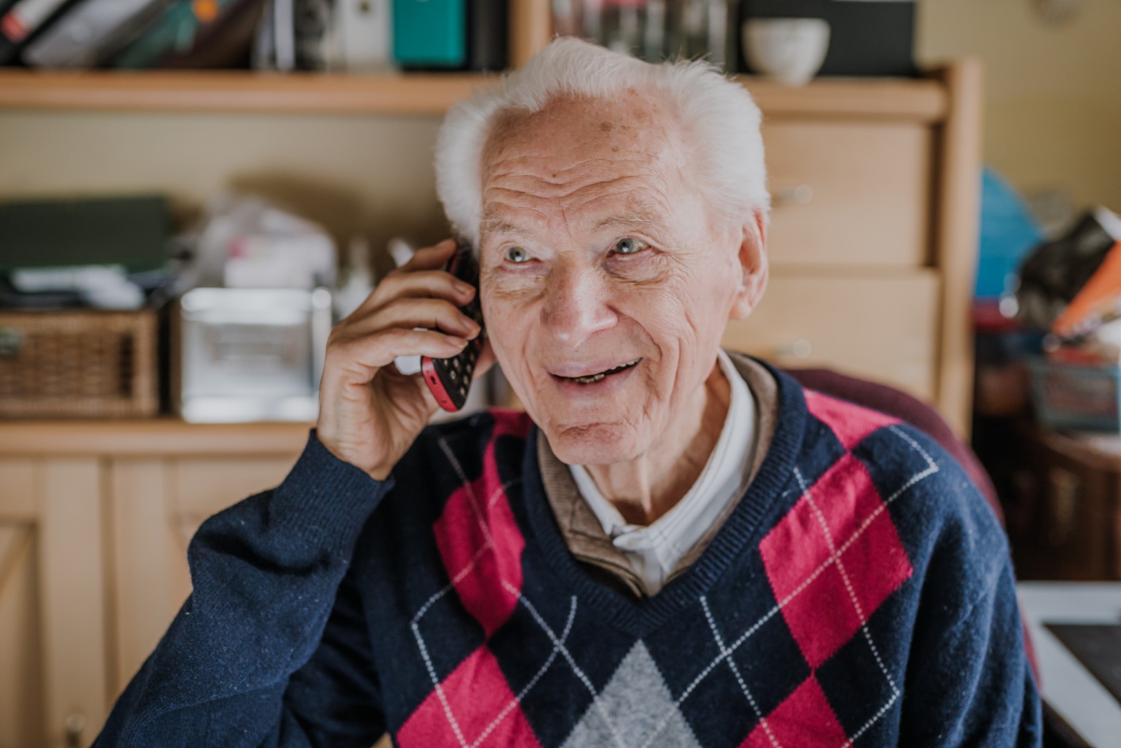 Photo of an elderly man representing Ray talking on a mobile phone in his home